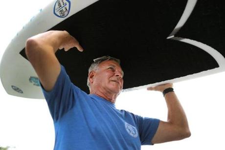Phil Clark, owner of Nauset Surf Shop, carried his new paddleboard into the shop to paint stripes on it, a shark deterrent tip he read about online.
