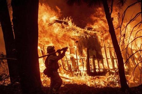 Firefighter Jose Corona sprays water as flames consume from the Camp Fire consume a home in Magalia, Calif..

