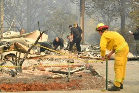 A CalFire firefighter set up tape as Yuba and Butte County Sheriff officers recover a body at a burned out residence in Paradise, California on Saturday.
