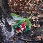 Flowers were placed Friday by neighbor Debbie Champigny near a tree where the burned remains of a body were found in Lynn. 