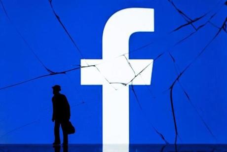 A figurine standing in front of Facebook?s logo, as seen on the cracked screen of a smartphone. 
