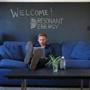 BOSTON, MA - 2/06/2019: Resonant Energy co-founder Isaac Baker works seated on a couch which they rehabilated, a slate table which an intern rehabilated with his feet ontop and a blackboard behind with the logo drawn on it. The company is a startup focused on providing solar power to low and middle income communities as well as non-profits including churches. Their office is in a wing of the 2nd Church of Dorchester, which they have installed solar panels on. (David L Ryan/Globe Staff ) SECTION: BUSINESS TOPIC xxworkspace