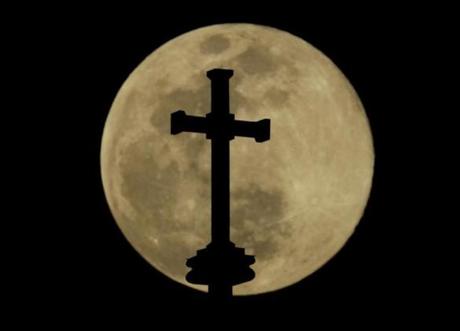A cross on top of the Holy Family Cathedral is silhouetted against the rising full moon Wednesday, March 20, 2019, in Tulsa, Okla. (AP Photo/Charlie Riedel)
