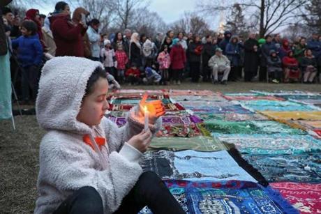 Esma, who chose to give her first name only, held a candle near the 50 symbolic prayer rugs representing the victims of the mosque killings in New Zealand at an interfaith vigil in Lexington.
