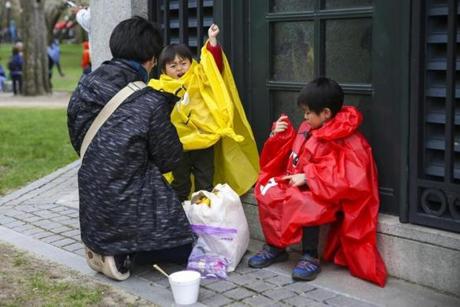 Takanori Kozuki (right), 6, and Hiroto Kozuki (center), 3, put on their ponchos before it began to rain Sunday. Expect dreary, cool conditions to prevail through the end of the week.
